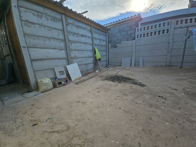 A rear outdoor area featuring precast concrete boundary walls and sandy ground, currently in an unfinished state requiring landscaping and maintenance.