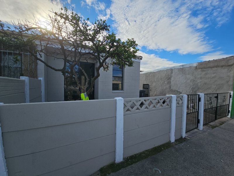 Front view of the property featuring a precast concrete boundary wall, metal pedestrian gate, and security bars on the windows.