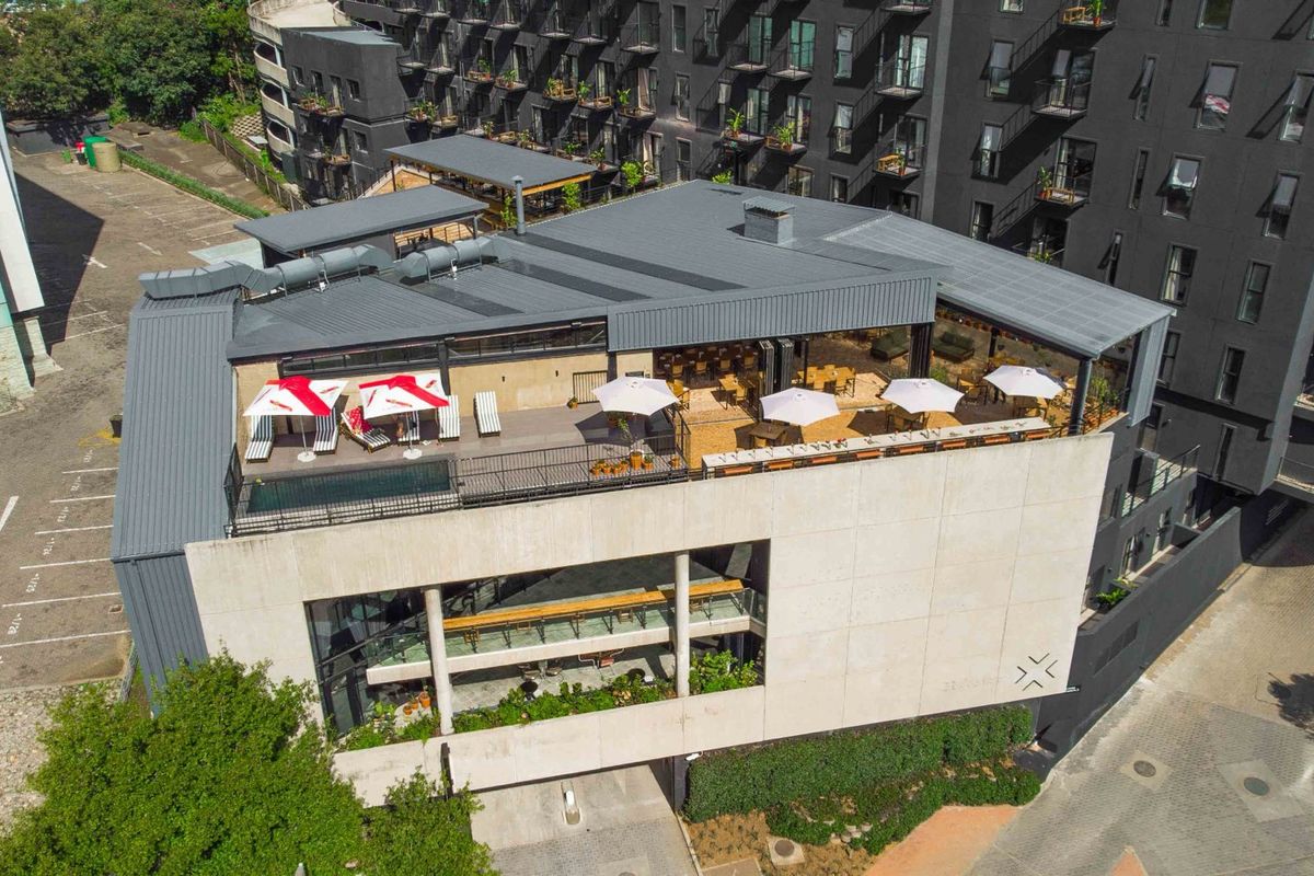 Aerial view of a modern apartment building featuring a rooftop terrace with a swimming pool, covered seating areas, and contemporary concrete and metal architecture.