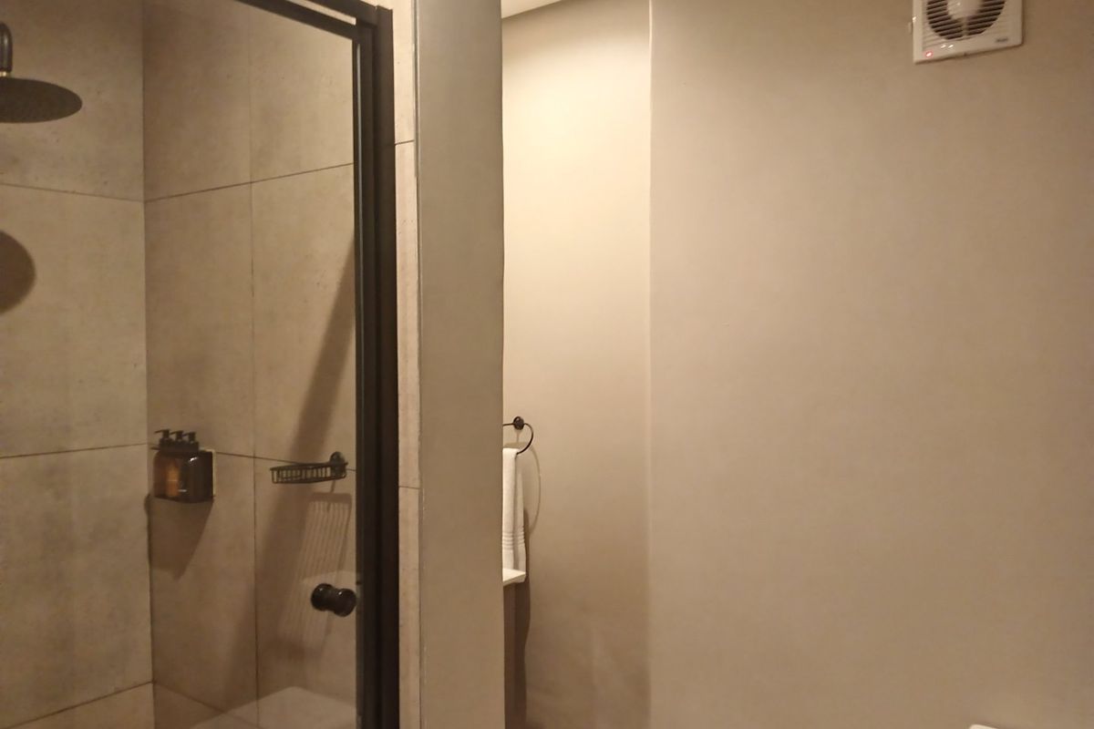 Modern bathroom featuring a walk-in shower with a black-framed glass screen, neutral wall finishes, and an integrated extractor fan.