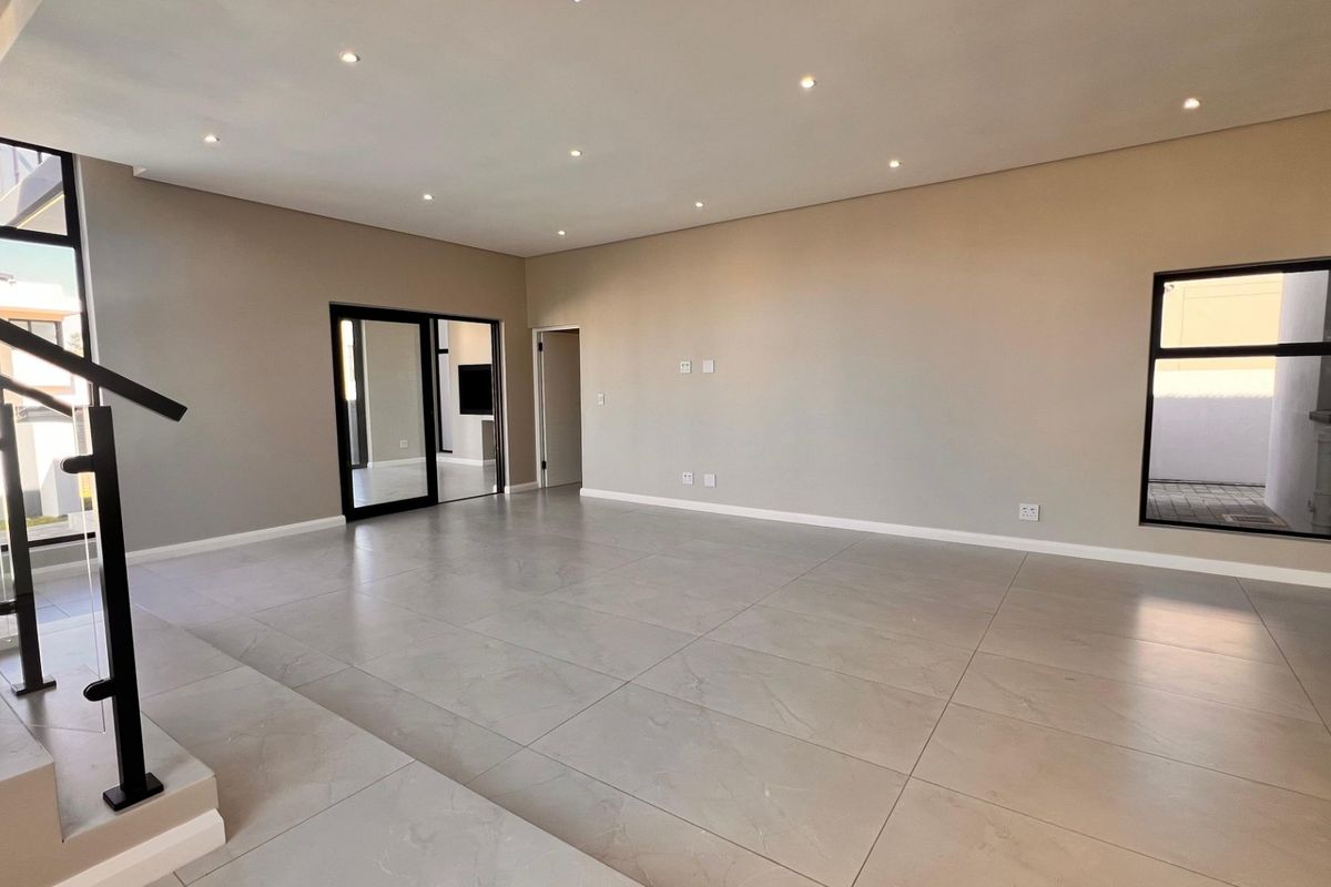 A spacious, modern open-plan living area featuring large-format porcelain floor tiles, recessed downlighting, and sleek black aluminium window and door frames.