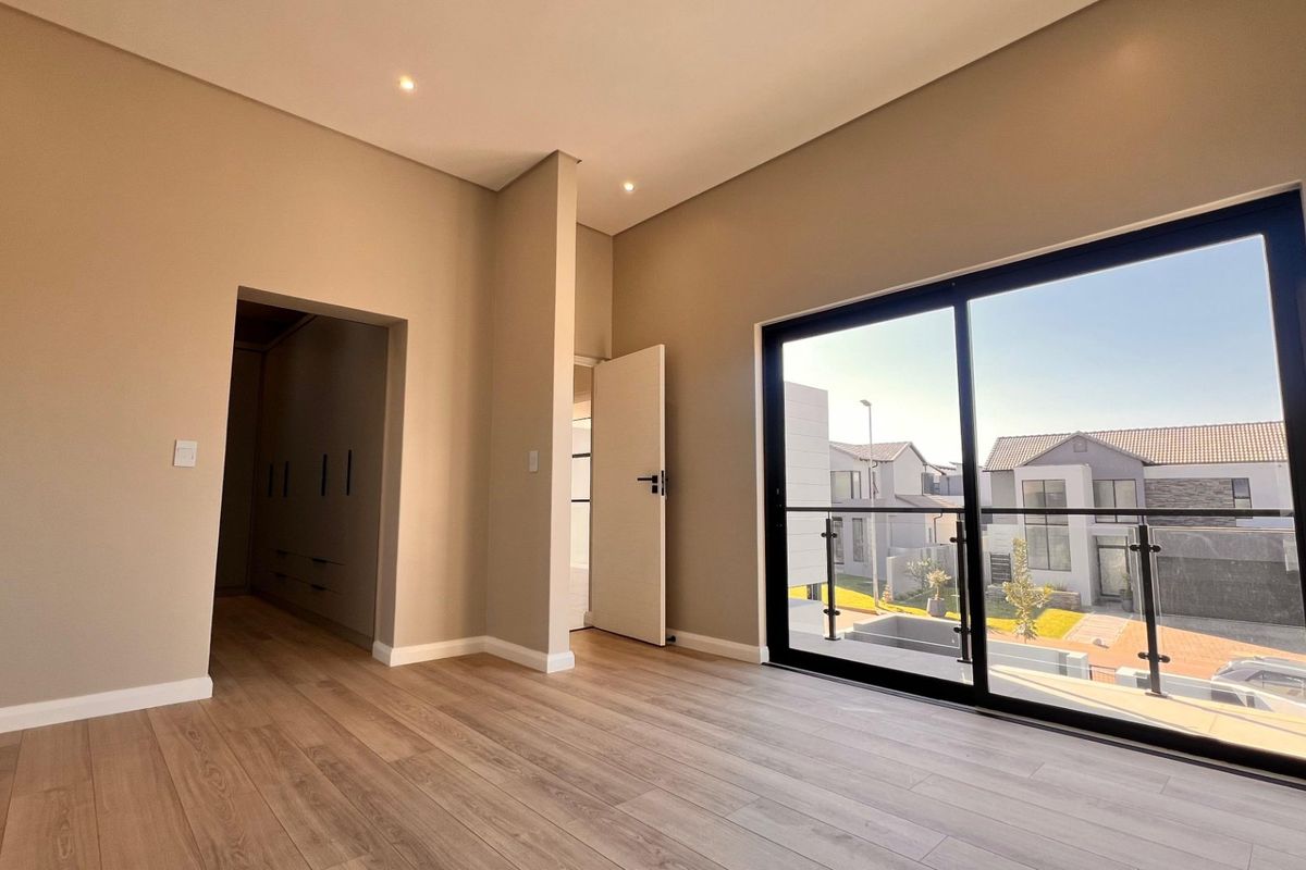 A bright, modern bedroom featuring laminate flooring, recessed lighting, and a large sliding door leading to a private balcony with neighborhood views.