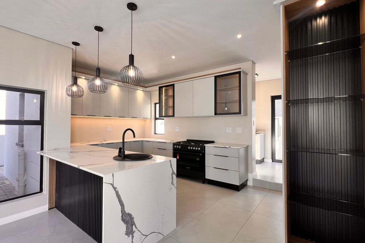 Modern kitchen featuring a marble-look stone island, black fixtures, gas stove, and sleek cabinetry with integrated lighting.