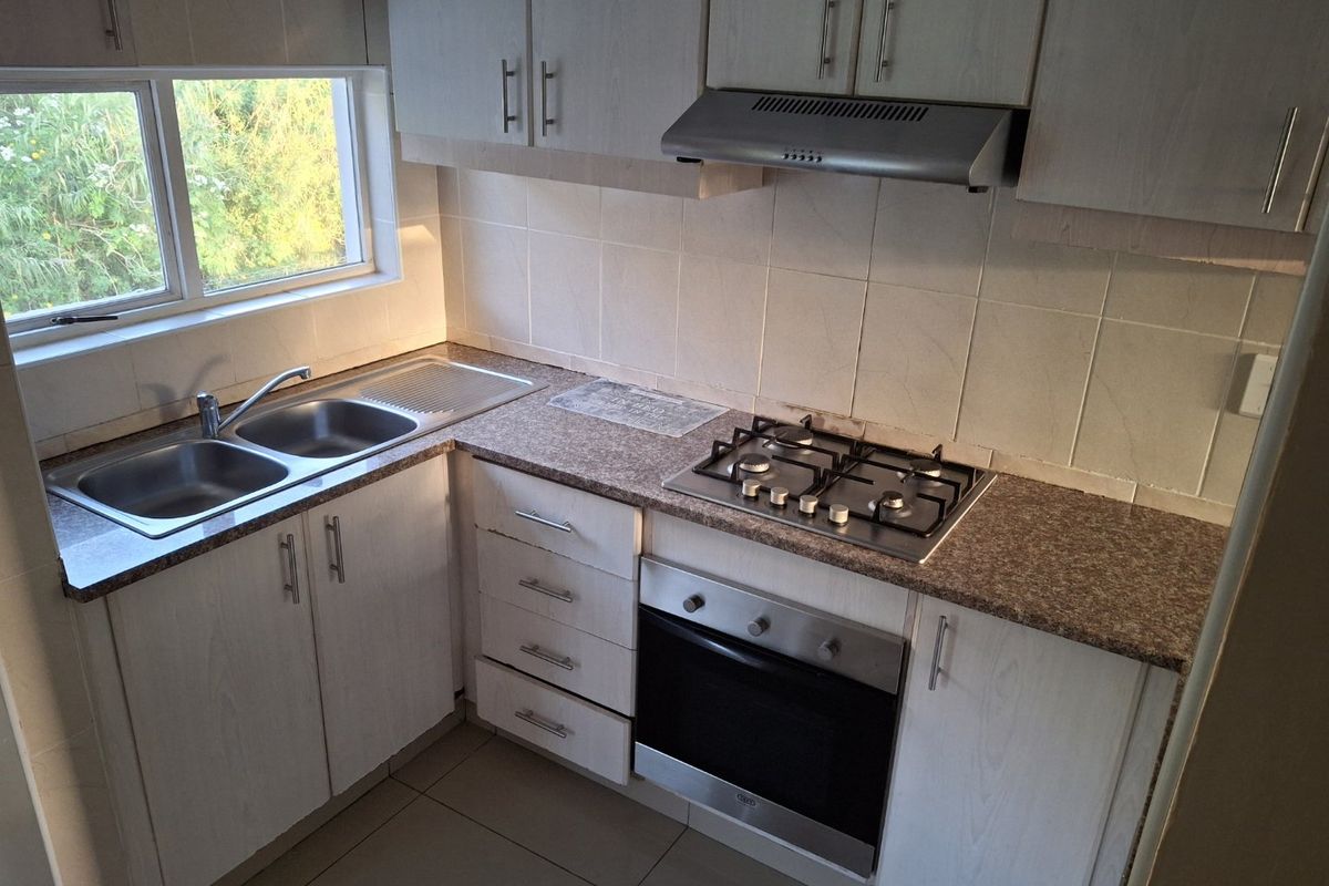 A functional kitchen featuring laminate cabinetry, a gas hob, built-in oven, extractor fan, and a stainless steel double sink with tiled backsplash.