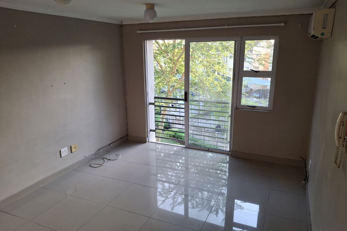 An empty living room featuring tiled floors, a sliding glass door leading to a balcony, and a wall-mounted air conditioning unit.