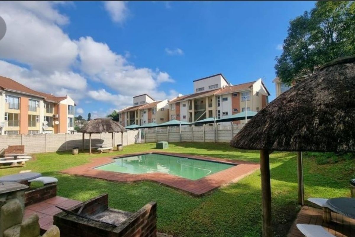 Communal pool area featuring a swimming pool, brick braai facilities, and thatch lapas within a secure apartment complex setting.