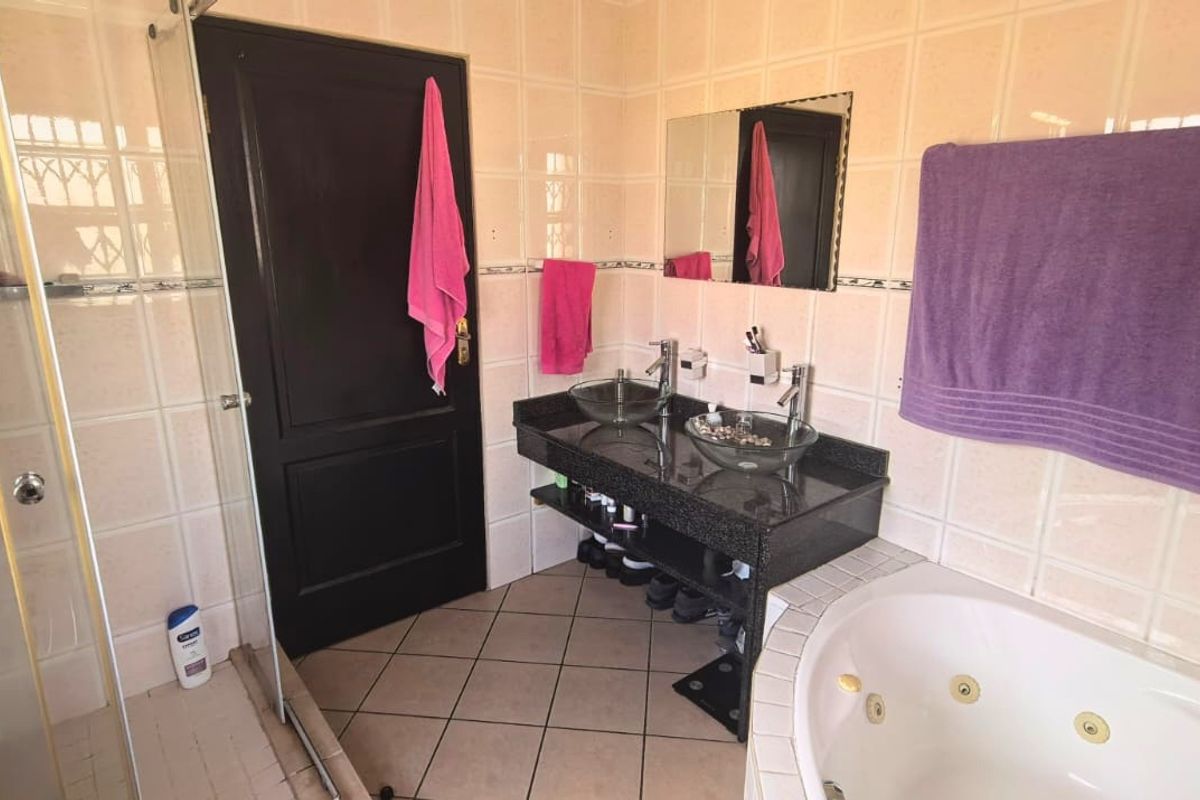 A functional bathroom featuring a double vanity with vessel sinks, granite countertop, glass shower enclosure, and a jetted bathtub with tiled finishes.