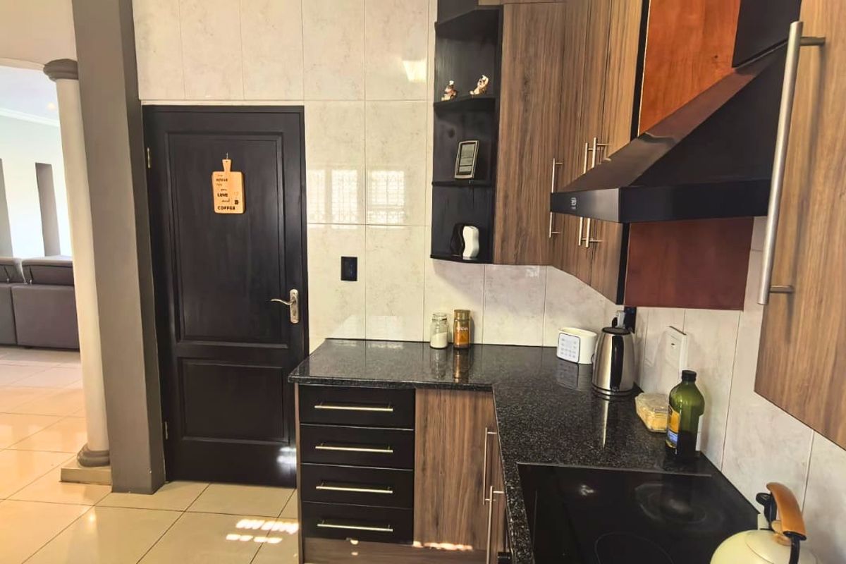 A functional kitchen featuring dark wood cabinetry, granite countertops, a built-in hob, and an extractor fan, with an open-plan flow to the living area.