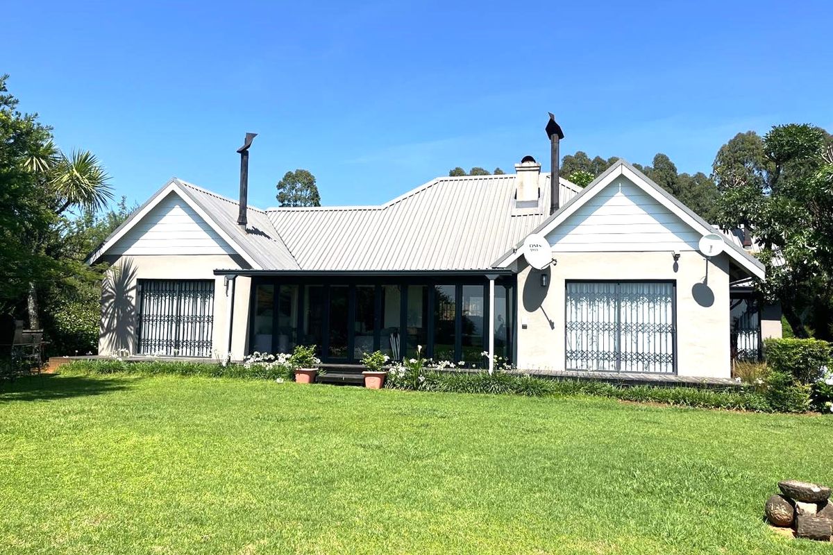 Rear view of a well-maintained house featuring a metal roof, covered patio, and expansive lawn area.