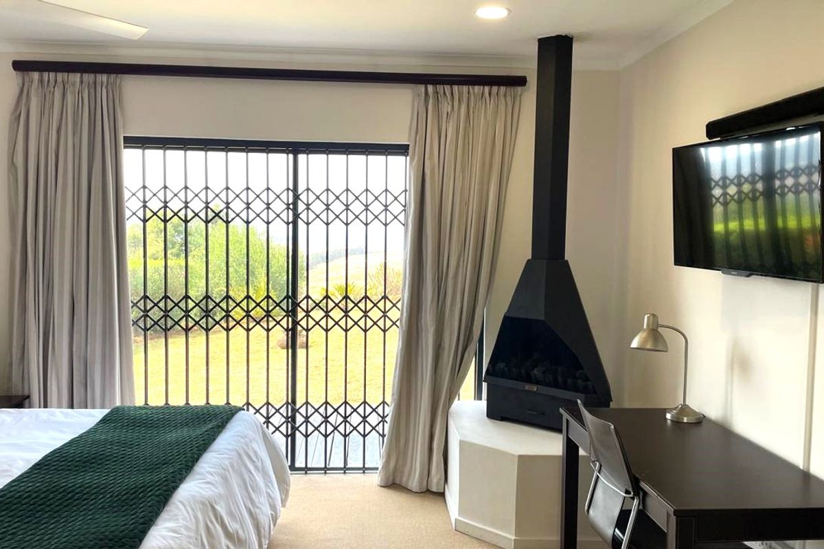 A comfortable bedroom featuring a modern freestanding fireplace, large sliding glass doors with security gate, and neutral carpeting.