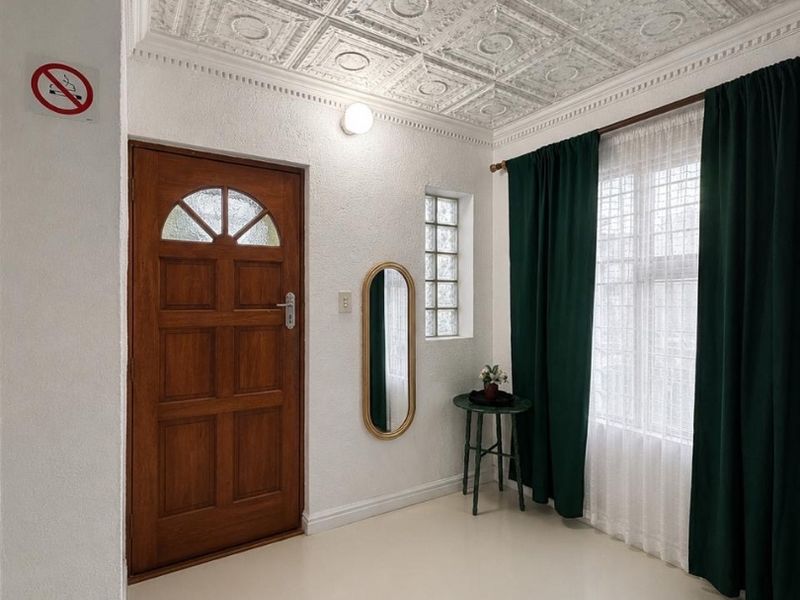 A bright entrance hall featuring a unique decorative tin ceiling, a solid timber front door, and a glass block window for natural light.