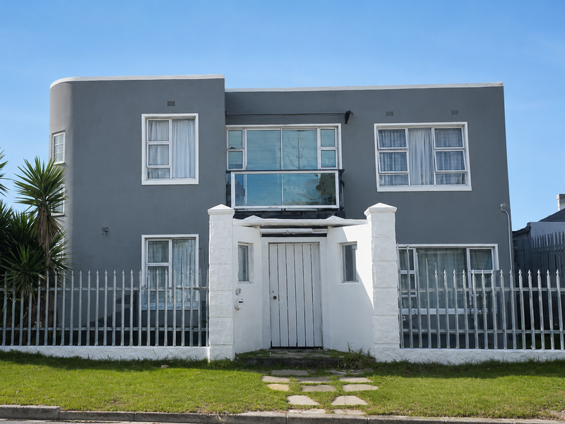 Front elevation of a two-story residence featuring a grey rendered facade, white perimeter fencing, and a central balcony with glass balustrade.
