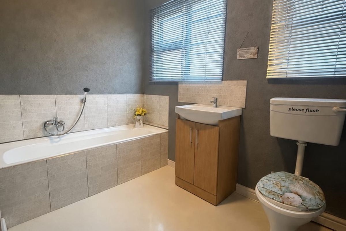 A functional bathroom featuring a built-in bathtub, vanity cabinet with basin, and a standard toilet, finished with grey walls and tiled splashbacks.