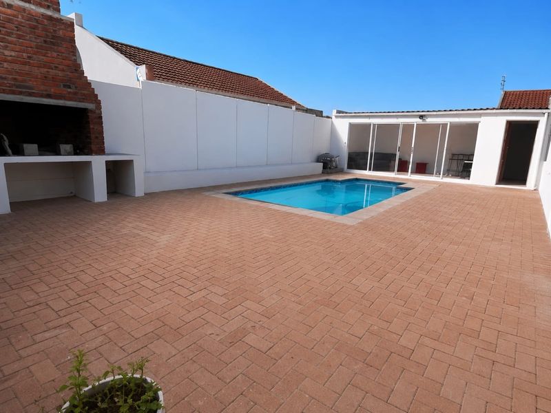 Outdoor entertainment area featuring a swimming pool, paved patio, and a built-in brick braai, perfect for hosting guests.