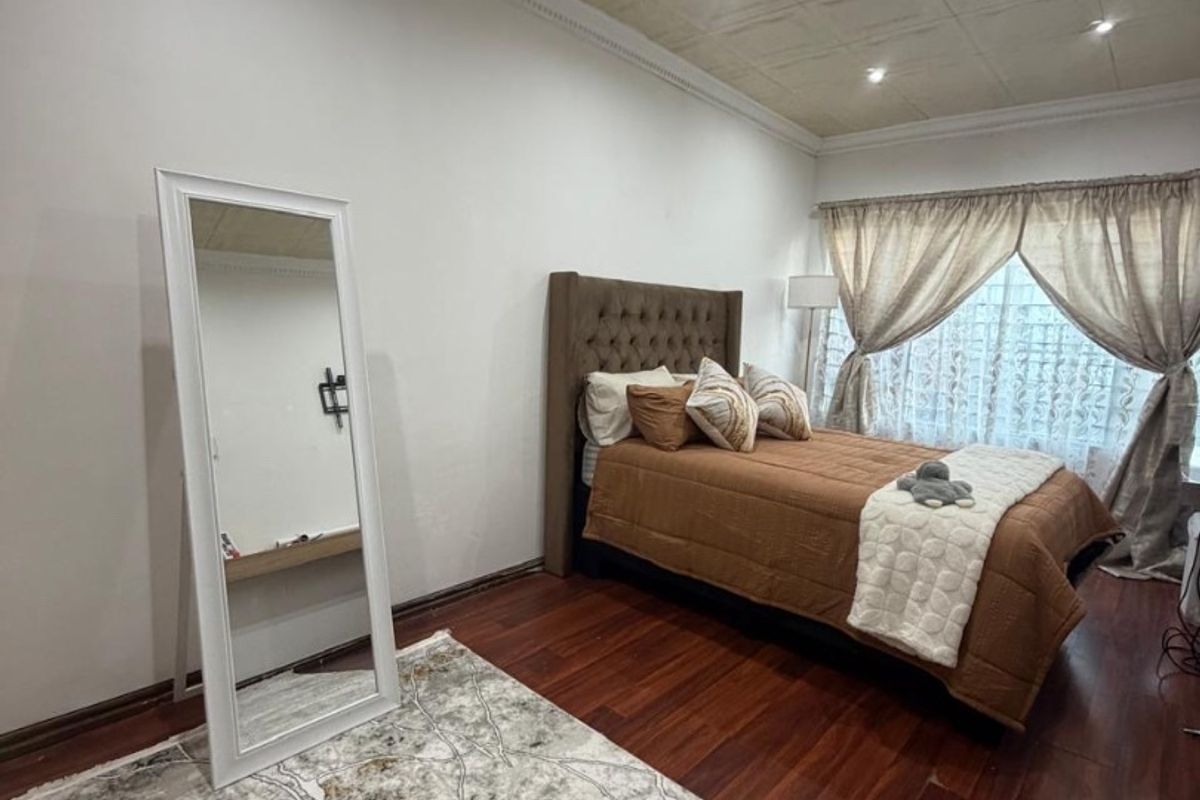 A well-maintained bedroom featuring rich hardwood flooring, a decorative coffered ceiling with recessed lighting, and elegant crown molding.