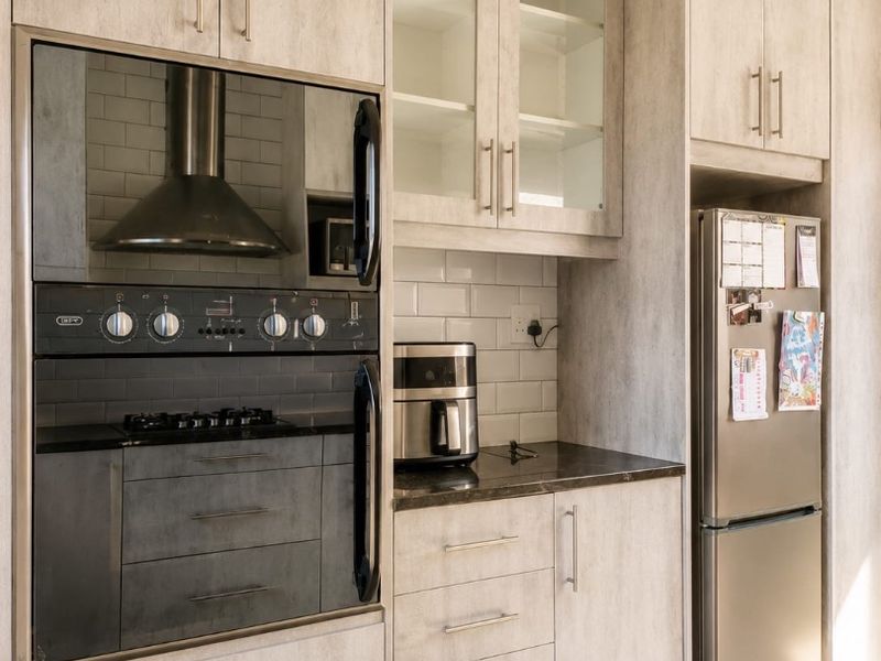 Modern kitchen featuring light wood-grain cabinetry, integrated oven and hob, subway tile backsplash, and a rustic exposed timber ceiling beam.