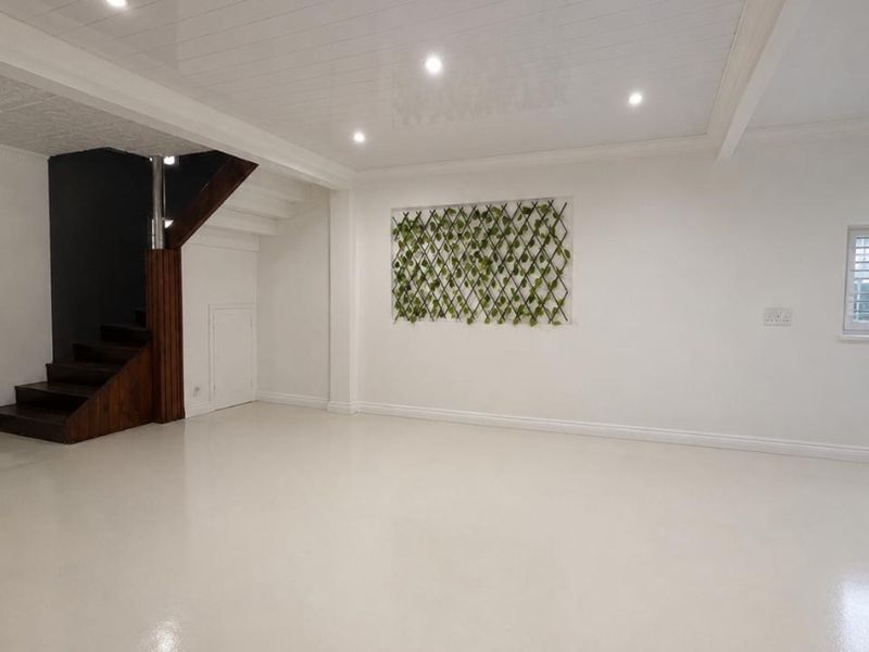 A bright, spacious living area featuring polished epoxy flooring, a modern timber staircase, and a clean white tongue and groove ceiling with recessed lighting.
