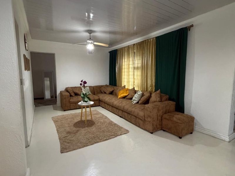 A spacious living room featuring a glossy painted concrete floor, a white tongue and groove ceiling, and a central ceiling fan.