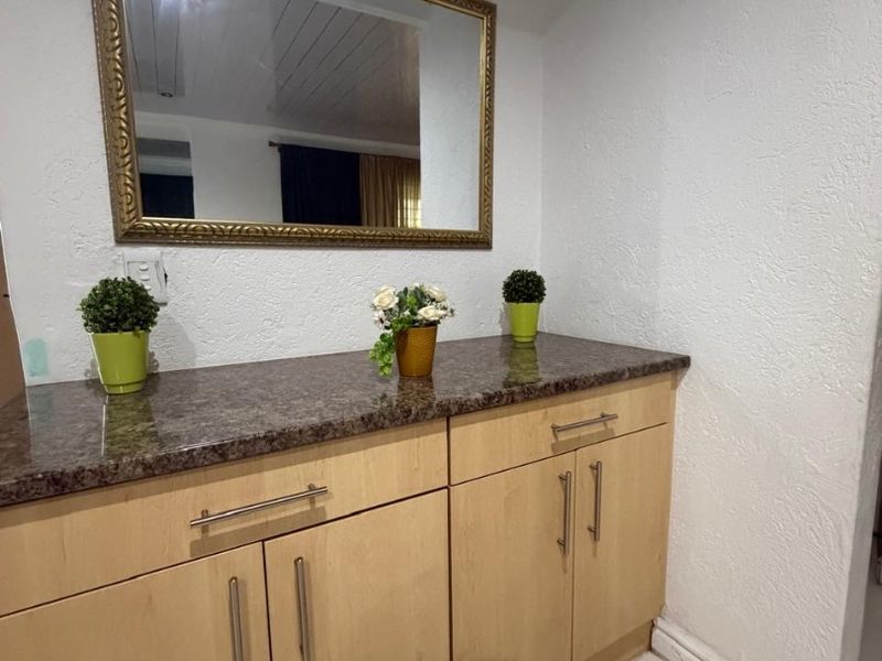 A functional utility space featuring light wood cabinetry, a durable granite countertop, and a decorative wall-mounted mirror.