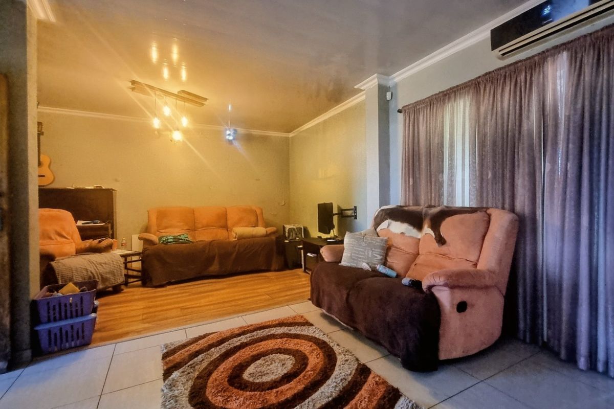 A spacious living area featuring a mix of tiled and laminate flooring, crown molding, and a wall-mounted air conditioning unit.