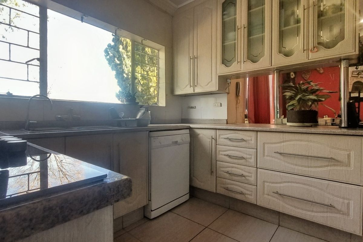 A functional kitchen featuring light-toned cabinetry, laminate countertops, tiled flooring, and a large window with security bars providing natural light.