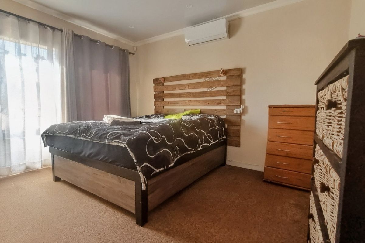 A carpeted bedroom featuring a wall-mounted split-system air conditioner and a sliding glass door providing access to the exterior.