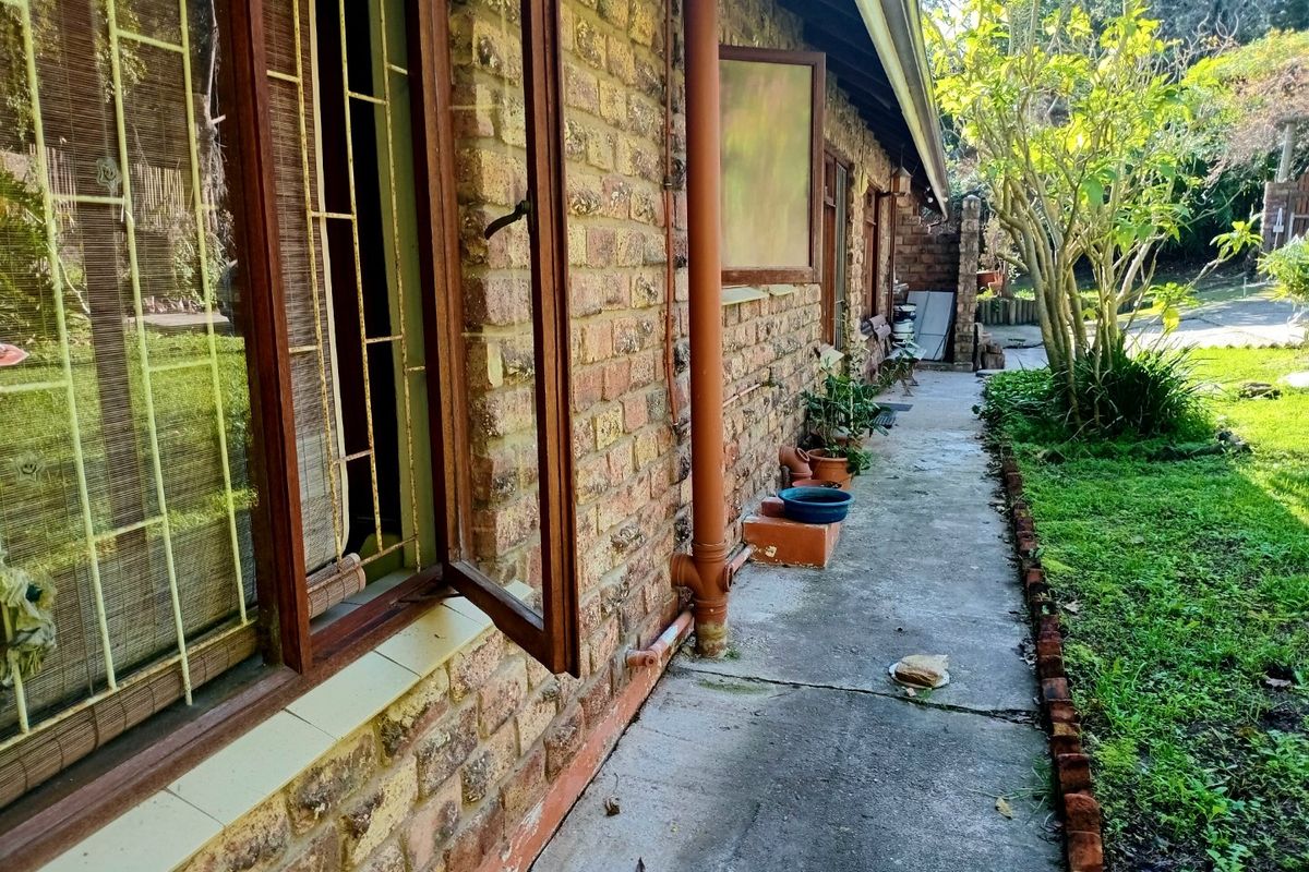 A view of the rear exterior of the house featuring face brick walls, timber window frames, and a concrete pathway leading along the side.