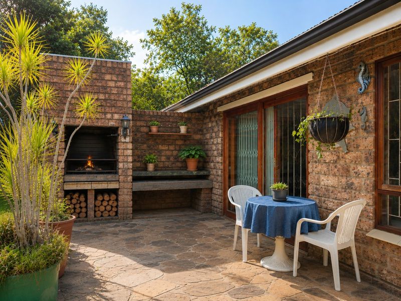 A well-maintained outdoor patio featuring a built-in brick braai, stone paving, and direct access to the home through sliding glass doors.