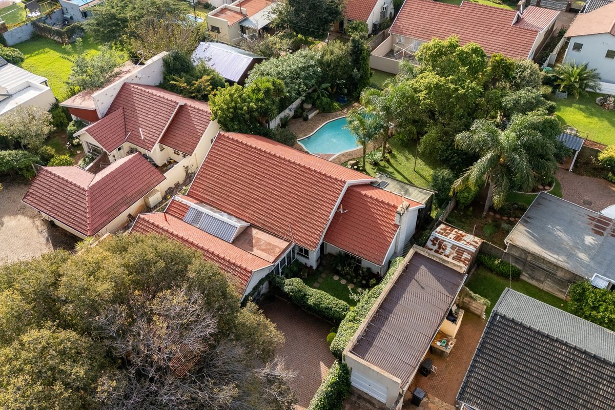 Aerial view of a residential property featuring a tiled roof, solar water heating, a swimming pool, and a paved driveway within a suburban setting.