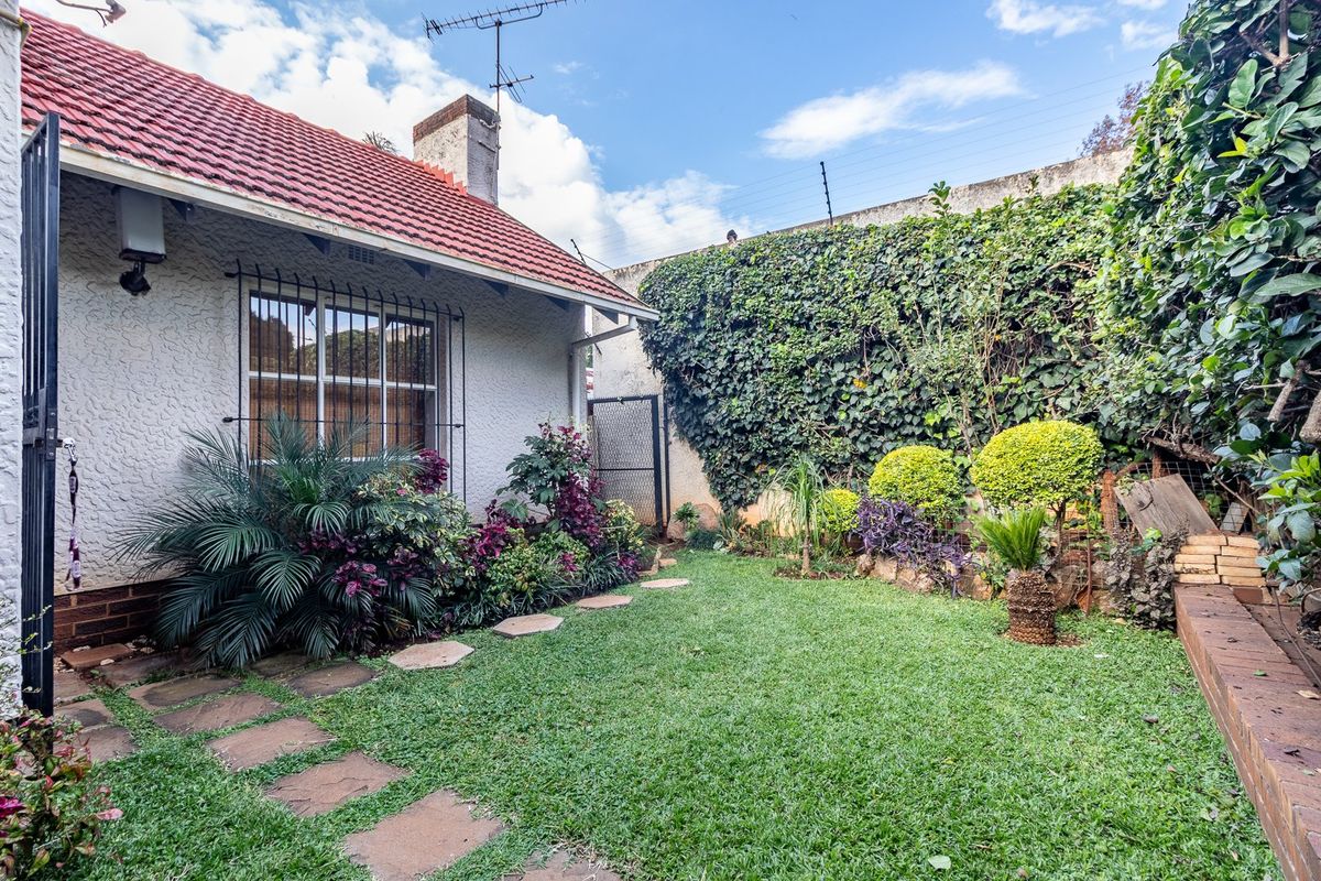A private rear garden featuring a lawn, paved pathway, and established perimeter landscaping with a secure boundary wall and electric fencing.