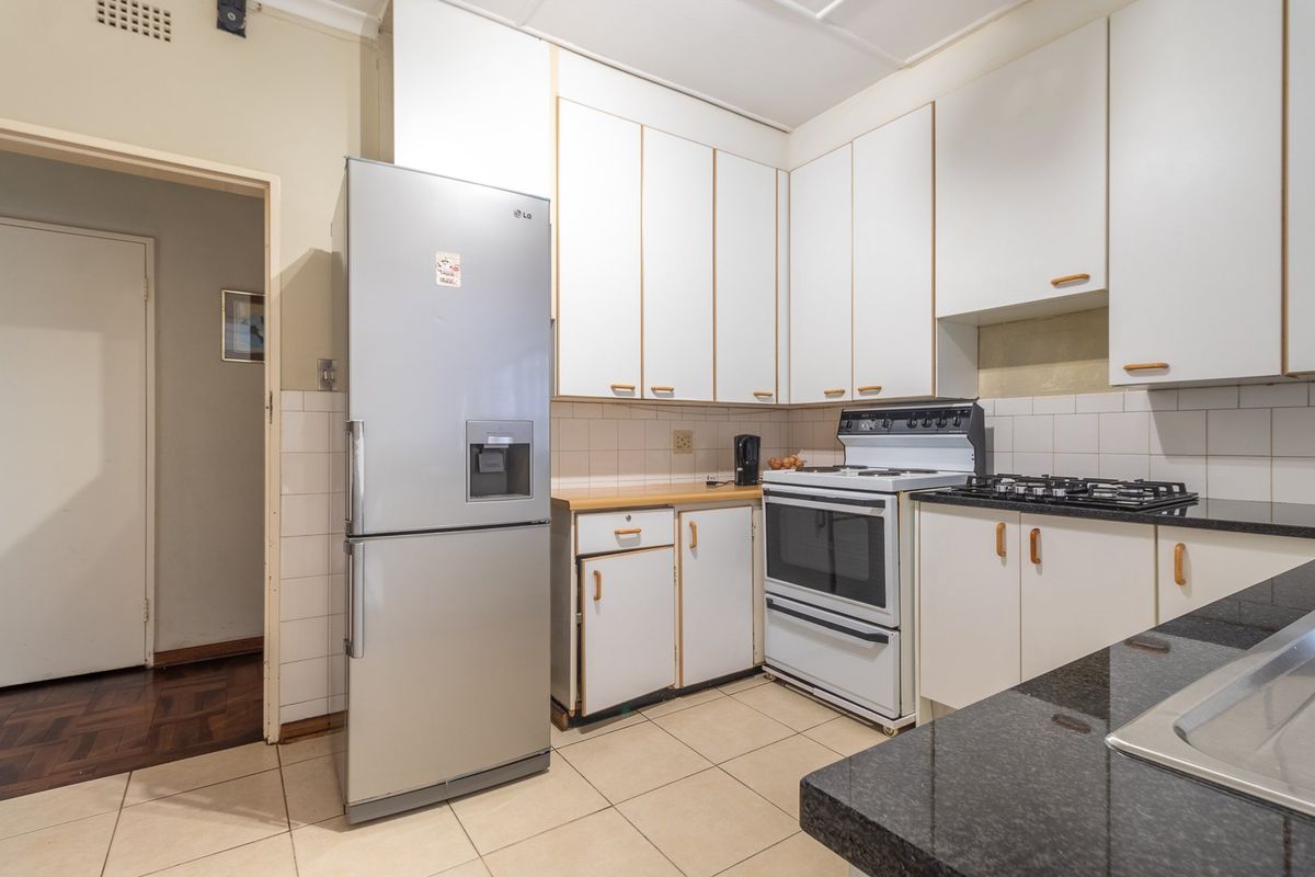 A functional kitchen featuring white cabinetry, granite countertops, tiled flooring, and a gas stove with an integrated extractor fan.