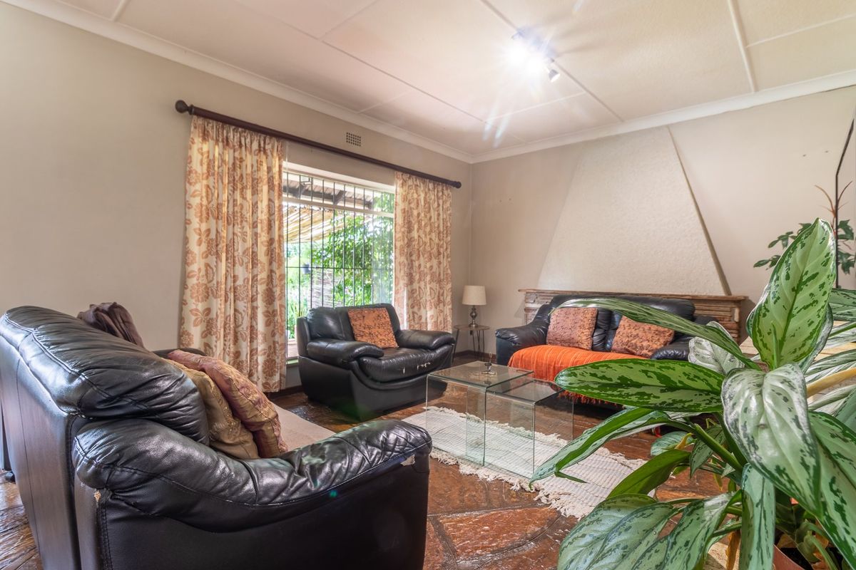 A living room featuring a prominent fireplace, natural stone flooring, and large windows with security bars, offering a traditional and cozy atmosphere.