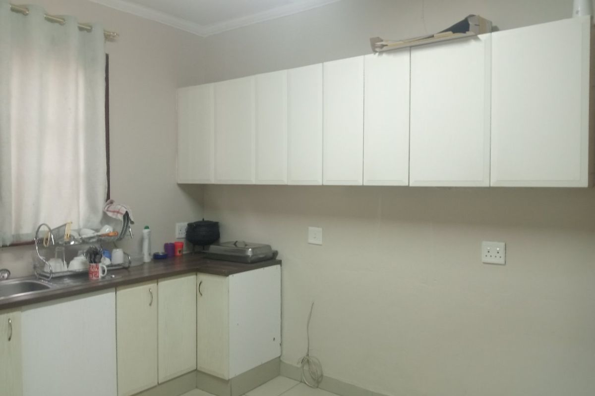 A functional kitchen area featuring white built-in cabinetry, laminate countertops, a stainless steel sink, and neutral tiled flooring.