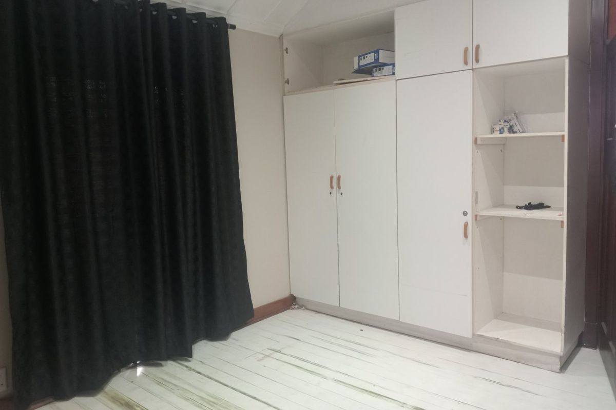 A bedroom featuring built-in white cabinetry and timber flooring, providing a functional storage solution in a neutral space.