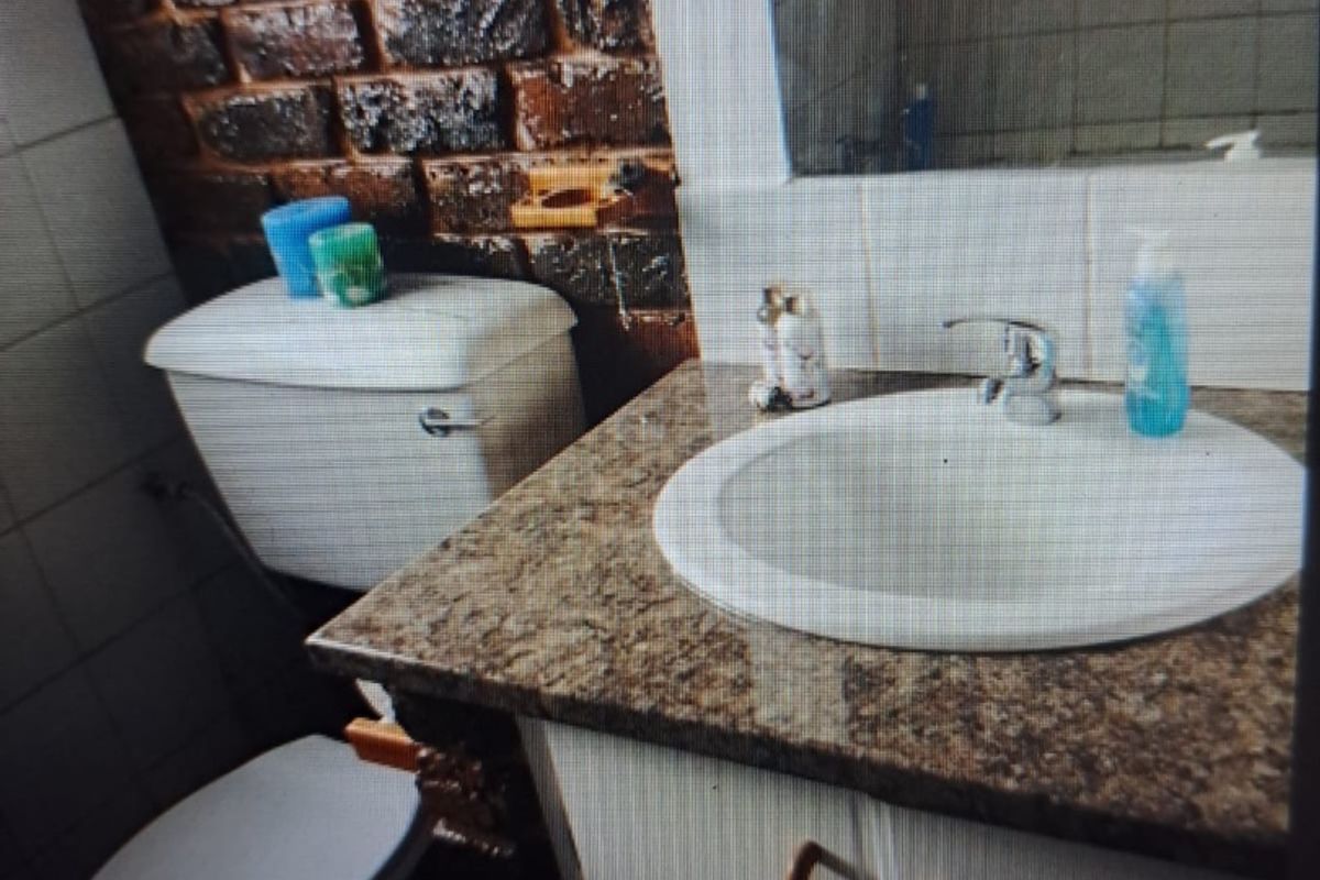 A bathroom featuring a granite-topped vanity, drop-in sink, toilet, and a distinctive exposed brick feature wall.