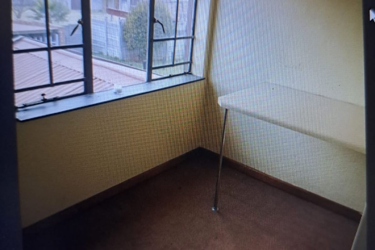 A compact bedroom featuring a built-in desk, steel-framed windows, and carpeted flooring, offering a functional space ready for modernization.