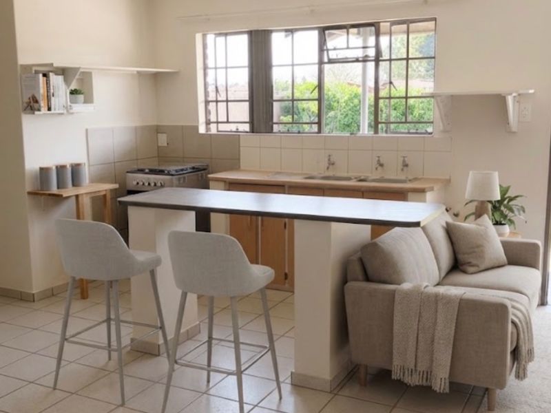 Open-plan kitchen and living area featuring tiled flooring, a breakfast counter, and functional built-in cabinetry with a classic steel frame window.