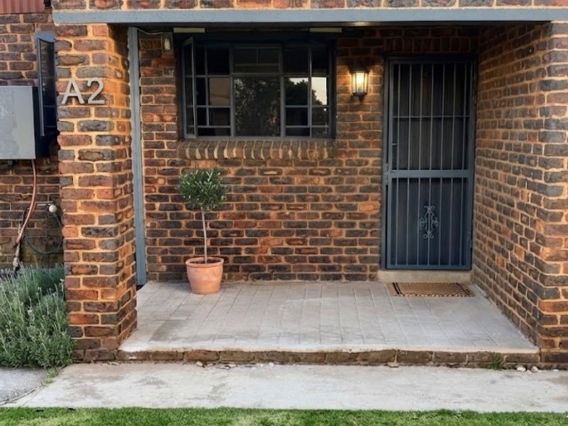 Front entrance of an apartment featuring a face brick facade, paved porch area, and secure metal gate entrance.