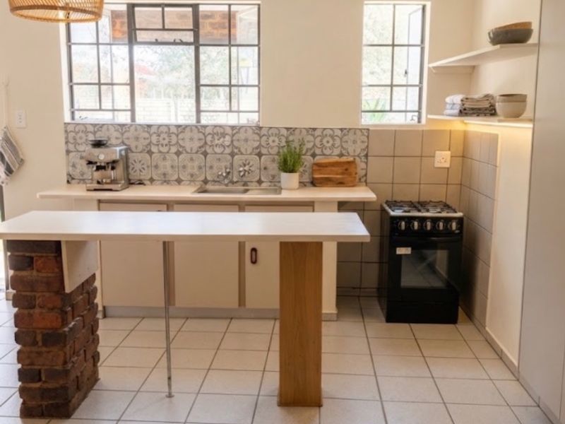 A bright kitchen featuring a tiled backsplash, gas stove, stainless steel sink, and a unique brick-based breakfast bar with ceramic floor tiles.