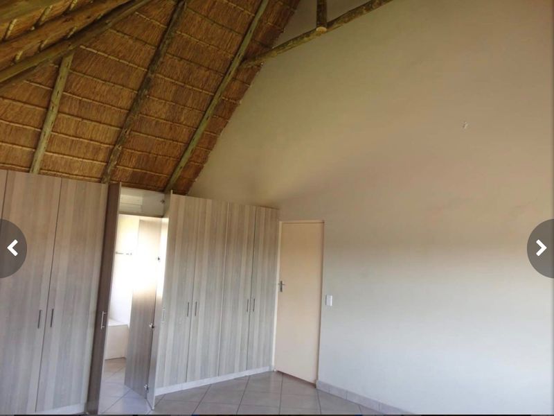 Spacious bedroom featuring a high vaulted thatch ceiling with exposed timber rafters, built-in cupboards, and neutral tiled flooring.