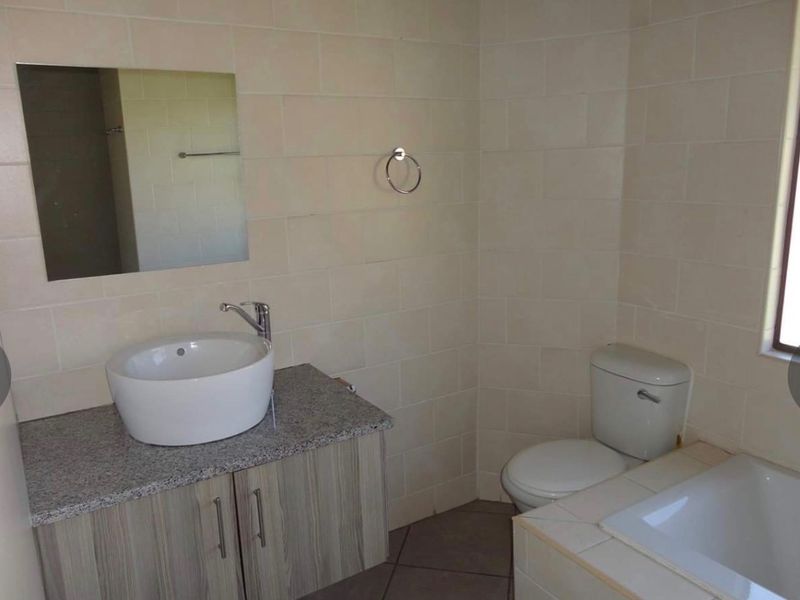 A clean, functional bathroom featuring a vessel sink on a granite vanity, a toilet, and a tiled bathtub area with neutral wall tiles.