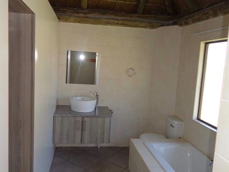 A bathroom featuring a vessel sink on a vanity cabinet, a built-in bathtub, and a unique exposed thatch roof ceiling.