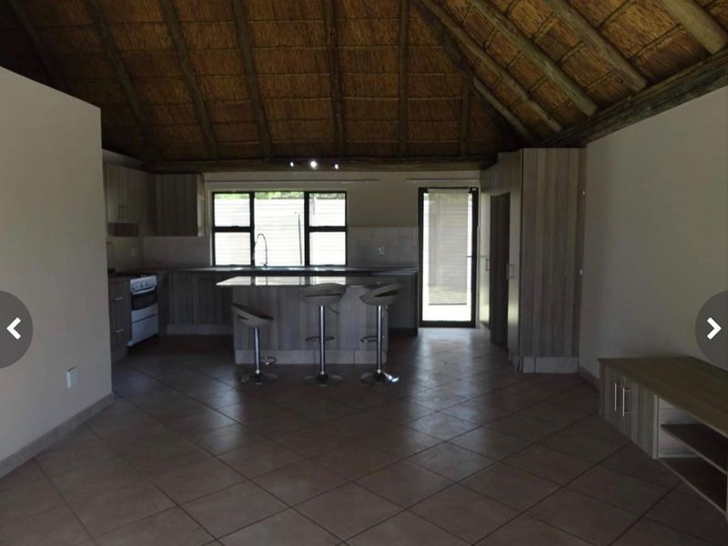 Open plan kitchen and living area featuring a high thatched ceiling, tiled flooring, and modern cabinetry with a central island.