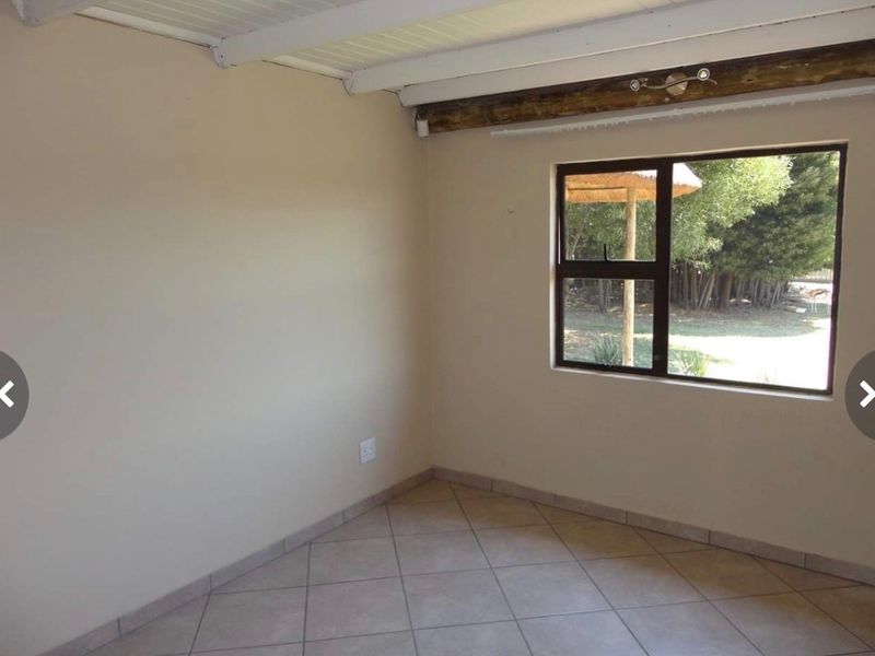 A vacant bedroom featuring tiled flooring, an exposed timber ceiling beam, and a large window overlooking the garden.