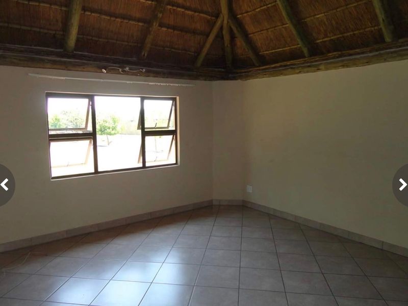 An empty living room featuring a traditional thatched roof with exposed timber rafters and neutral tiled flooring.