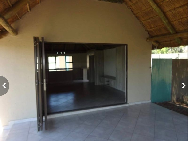 Covered patio area featuring a traditional thatched roof, tiled flooring, and large stacking doors opening into the main living space.