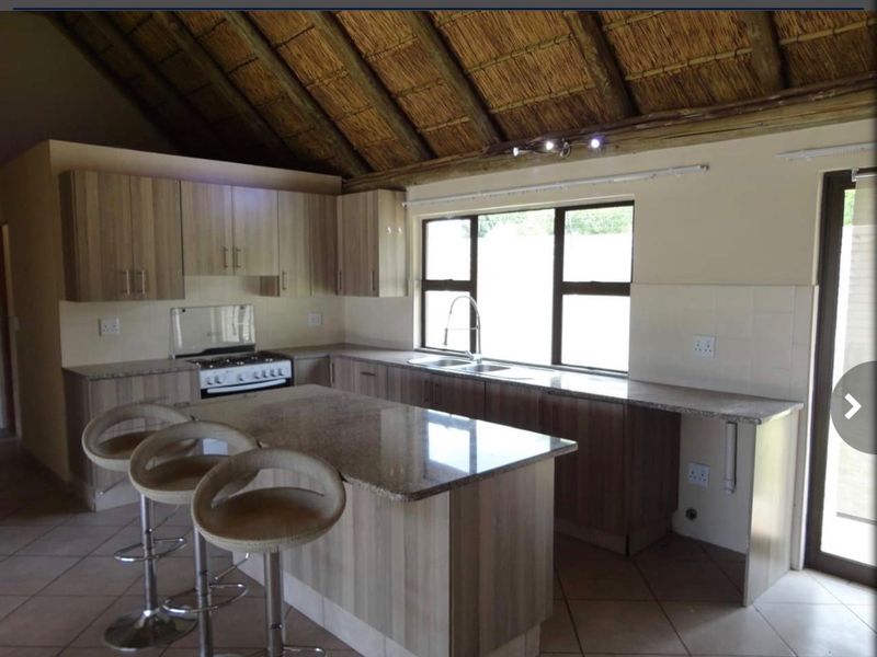A functional kitchen featuring granite countertops, built-in cabinetry, a gas stove, and a distinctive exposed thatch roof ceiling.