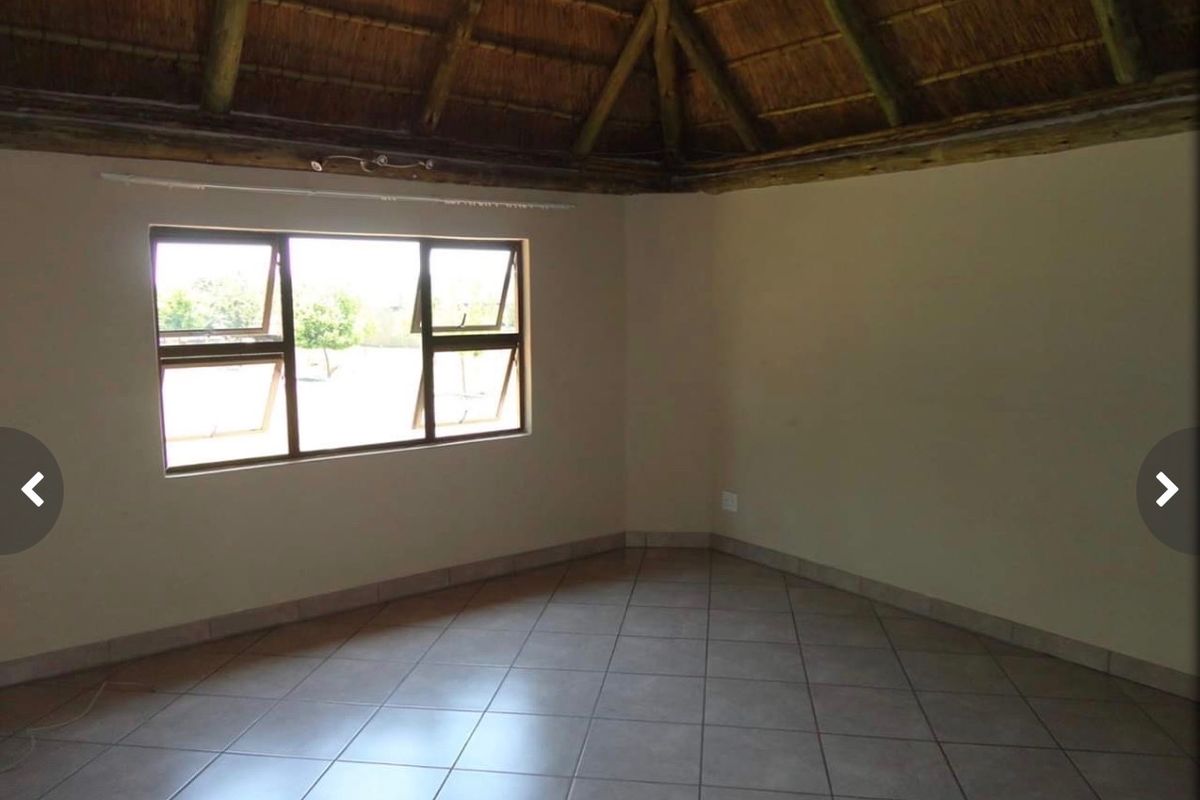 An empty living room featuring a traditional thatched roof with exposed timber rafters and neutral tiled flooring.