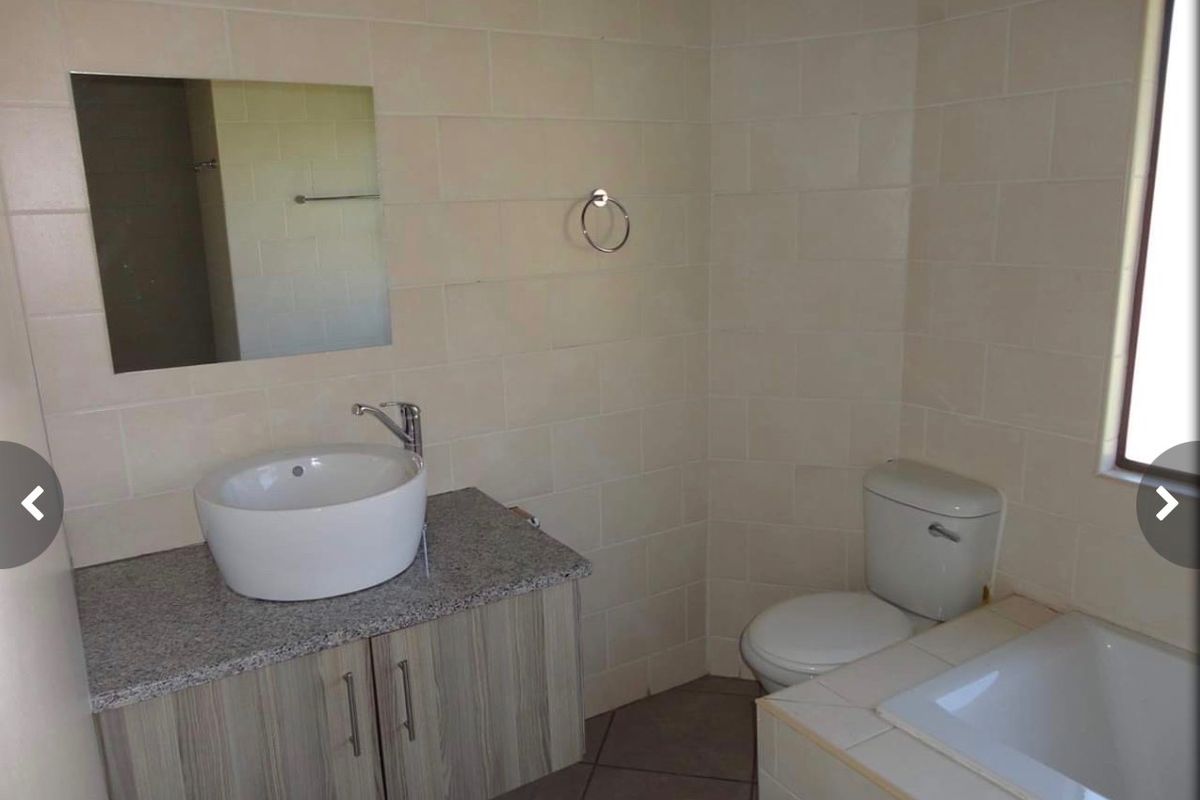 A functional bathroom featuring a vessel sink on a granite vanity, a built-in bathtub, and neutral ceramic wall tiling.