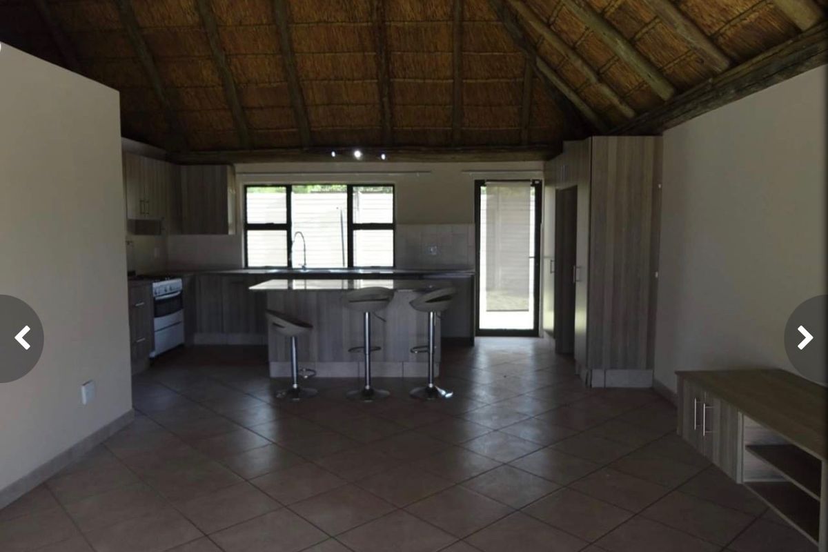 Open-plan kitchen and living area featuring a high thatched ceiling, tiled flooring, and a central kitchen island with built-in cabinetry.